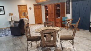 Un comedor con una mesa redonda y cuatro sillas de mimbre, un sofá oscuro y una alfombra estampada.