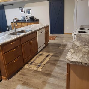 A kitchen with wooden cabinets, a granite countertop, a dishwasher, a stove, and a blue door.