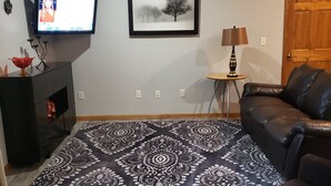 Una sala de estar con un alfombra estampado, un televisor, un cuadro enmarcado, una lámpara y una puerta.