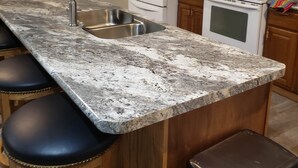 Una cocina con encimera de granito, pileta de acero inoxidable, gabinetes de madera, refrigerador blanco, microondas y estufa.