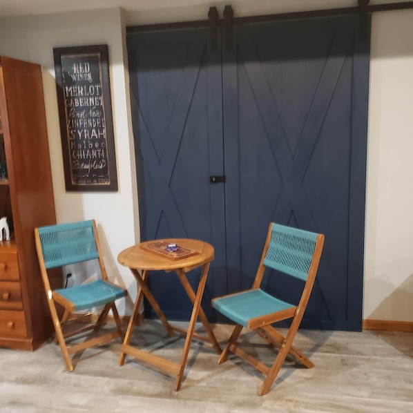 Een kamer met een blauwe deur, twee houten stoelen met blauwe kussens en een klein houten tafeltje.