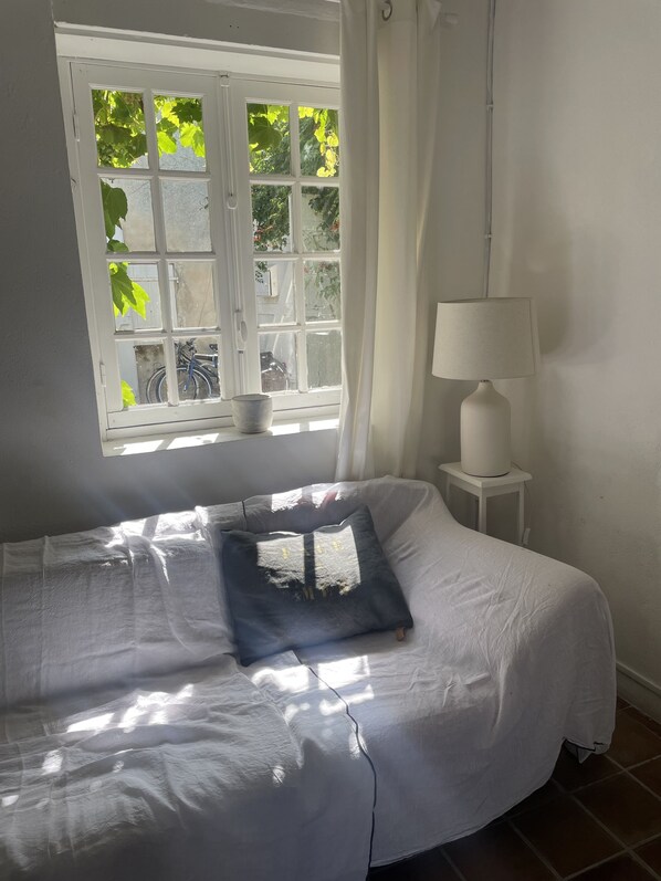 Ein Schlafzimmer mit Bett, einem Fenster mit Vorhängen, einer Nachttischlampe und Blick ins Grüne.