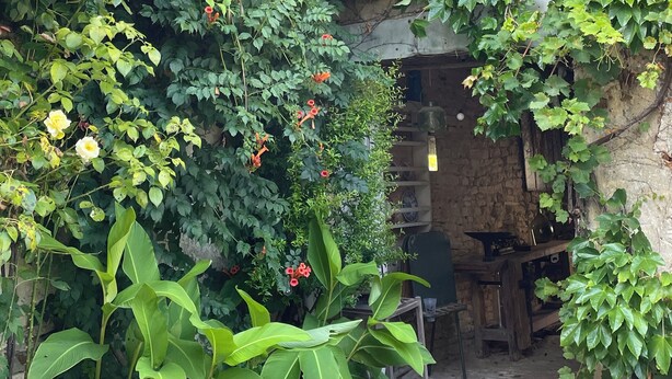 Un jardin avec un mur de pierres, un banc en bois et un bâtiment à l’aspect rustique.