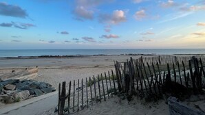 Une plage avec une clôture en bois, une zone rocheuse et l’océan en arrière-plan.