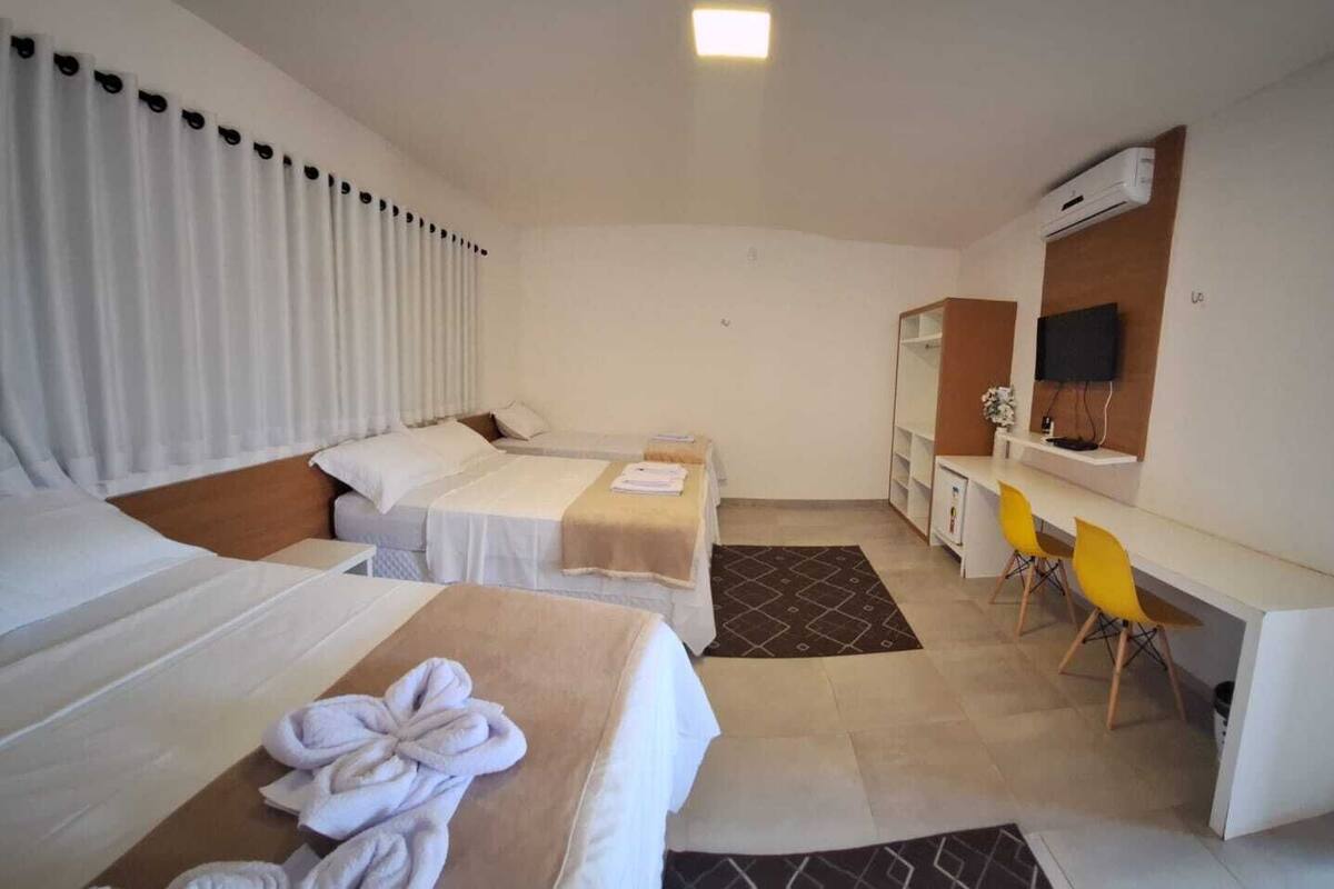 A hotel room with two beds, a desk with a chair, a mirror, and a small TV.