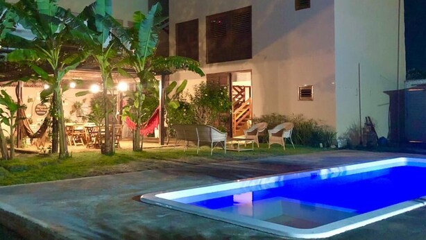 A modern building with a swimming pool, outdoor seating, and tropical plants.