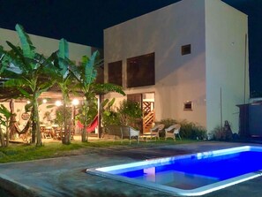 Un edificio moderno con piscina, asientos al aire libre y plantas tropicales.