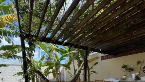 An outdoor dining area with a table set for two, surrounded by wooden chairs, under a pergola with a view of the sea.
