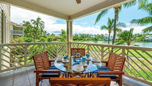 Un espace extérieur abrité, aménagé pour les repas, avec une table en verre et des chaises en bois, offrant une vue sur une piscine et une végétation luxuriante.