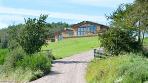 Een modern landhuis met twee verdiepingen en een grindpad dat leidt naar een houten poort.