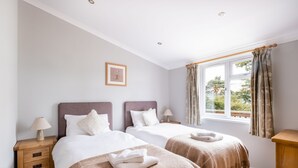 Een hotelkamer met twee bedden, een raam met gordijnen, een nachtkastje met een lamp en een ingelijst schilderij aan de muur.