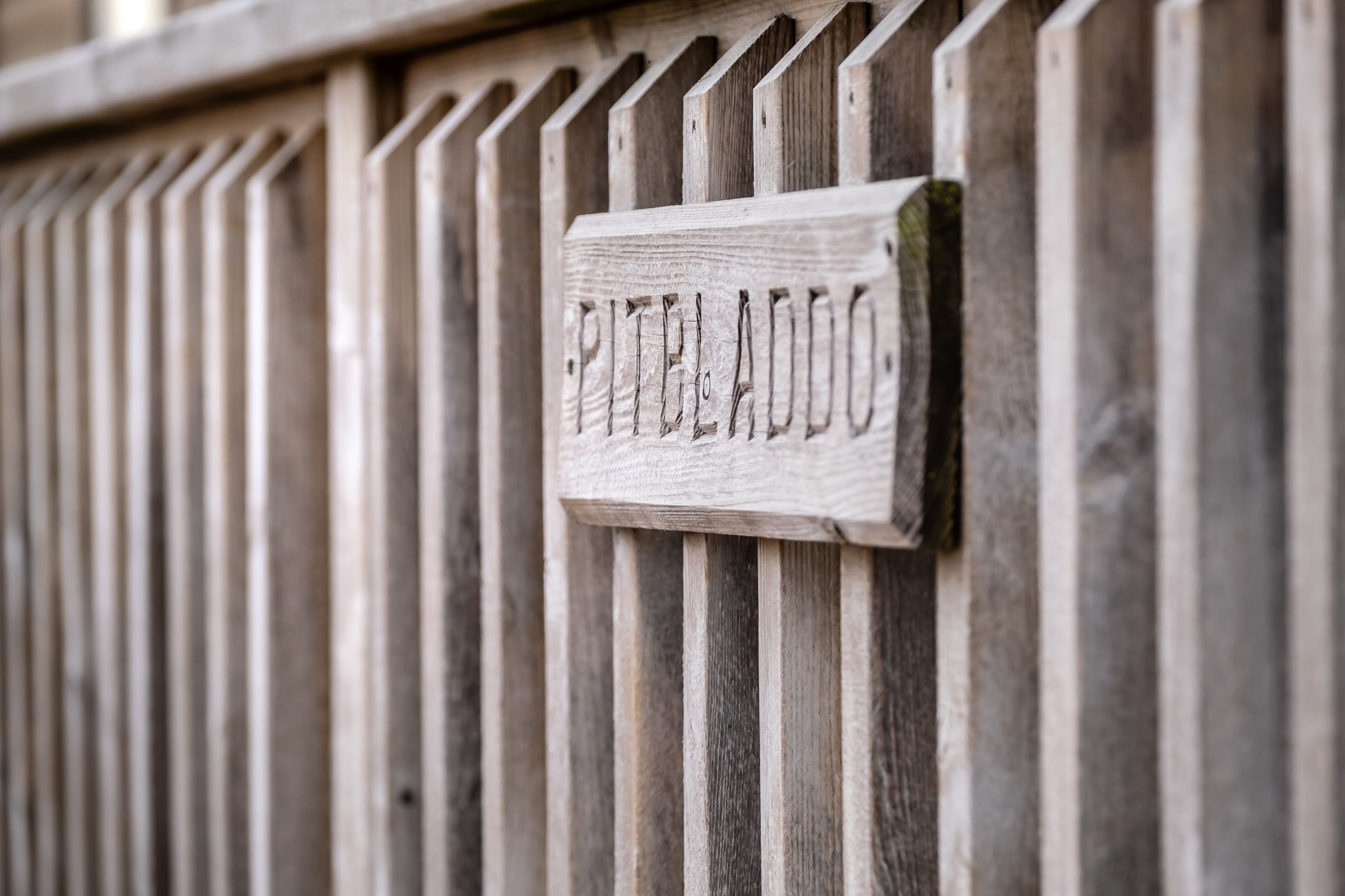 A wooden sign with the name "PITELLO ADOO" mounted on a wooden fence.