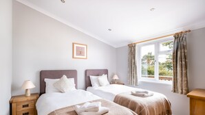 Habitación de hotel con dos camas, una ventana con cortinas, una mesita de noche con lámpara y un cuadro enmarcado en la pared.