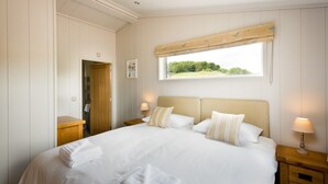 Een netjes opgemaakt slaapkamer met een groot bed, twee nachtkastjes, een raam met uitzicht op groen en een houten deur.
