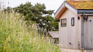 Een houten blokhut met een mosgroen dak, omringd door hoog gras en bomen.