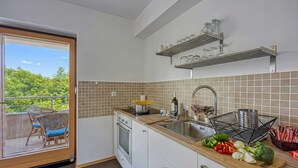 Une cuisine avec une porte-fenêtre coulissante donnant sur un balcon, un évier et un plan de travail avec des légumes.