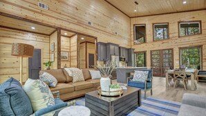 A spacious living area with a wooden ceiling, a brown sofa, a coffee table, and a dining area with a table and chairs. - Forever In Blue Jeans in Hochatown/Broken Bow,OK (Broken Bow)