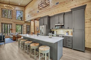 Une cuisine spacieuse dotée d’un grand îlot central, de meubles gris et d’un plafond en bois.