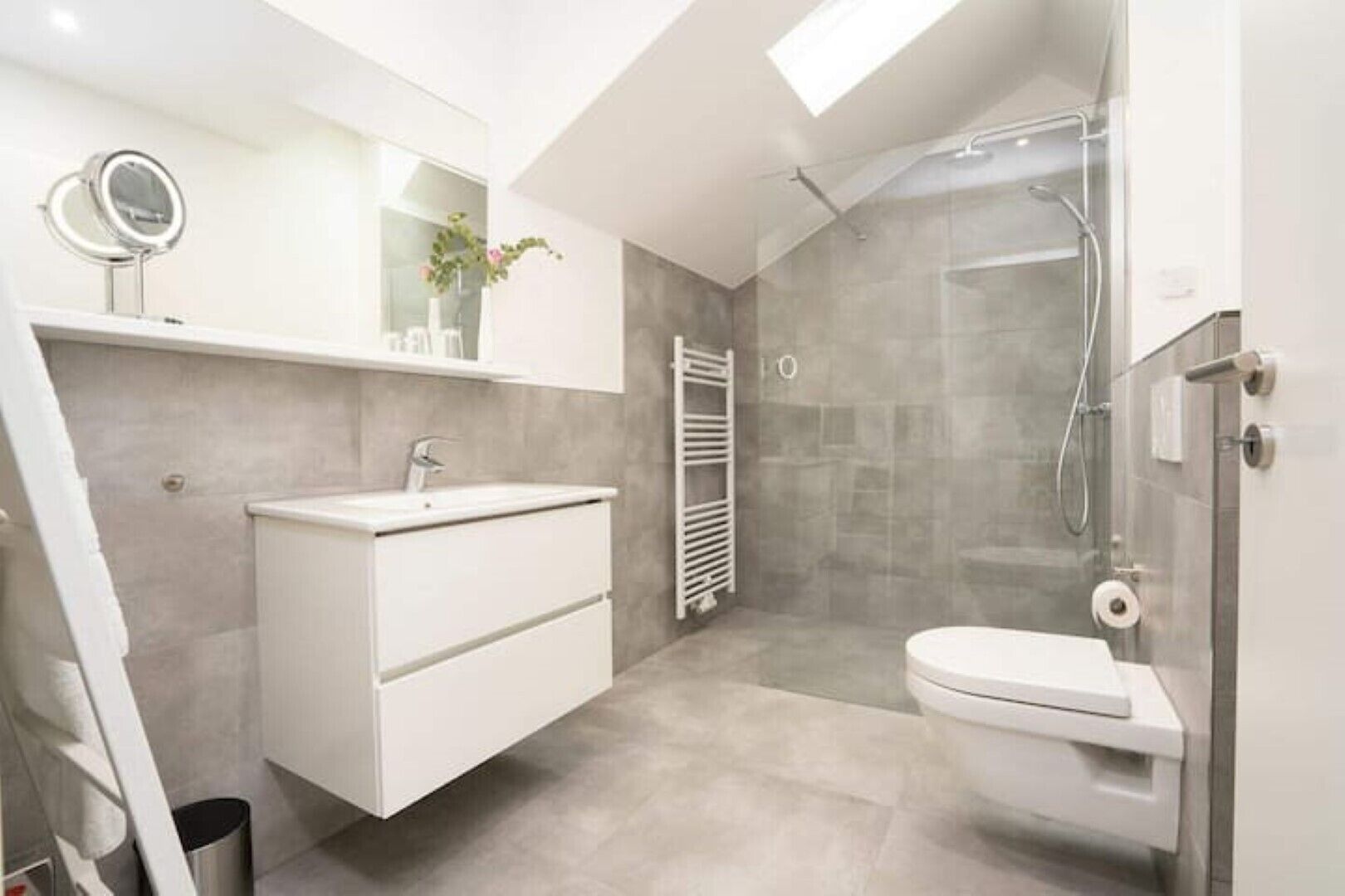 Et moderne badeværelse med et hvidt underskab, toilet, brusebad og ovenlys.
