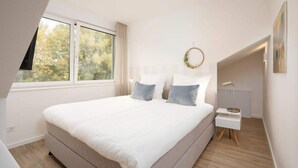 Une chambre à coucher avec un grand lit, une fenêtre, une table de chevet et une lampe fixée au mur.