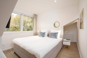 Une chambre à coucher avec un grand lit, une fenêtre, une table de chevet et une lampe fixée au mur.