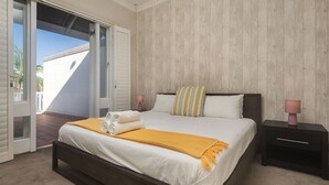 Een slaapkamer met een bed, nachtkastjes, een houten wand en een open deur naar een balkon.