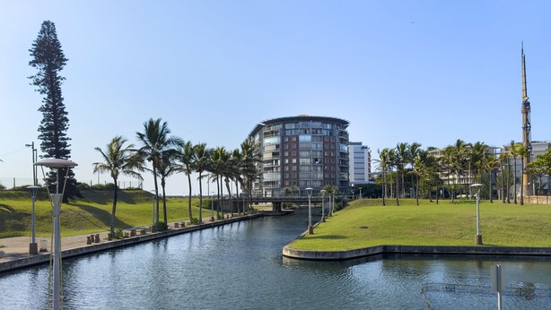 Een hotel aan het water, met een kanaal, palmbomen en een modern gebouw met balkons.