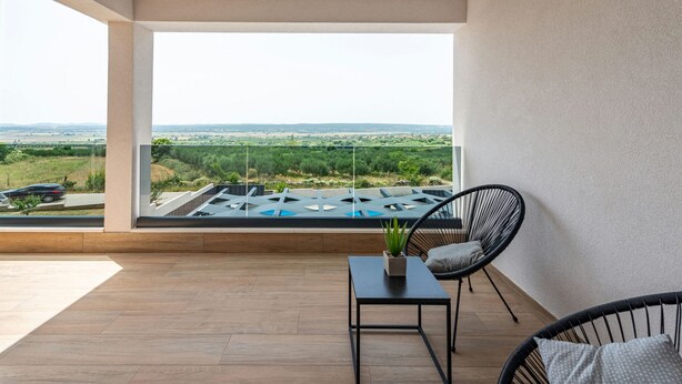 Un balcon avec vue sur un paysage verdoyant et une piscine. On y trouve une table avec une plante et deux chaises.