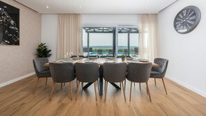 Un coin repas avec une table dressée pour six personnes, de grandes fenêtres offrant une vue dégagée et une horloge au mur.