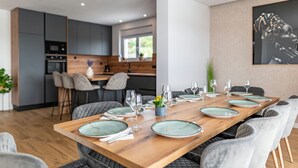 Un espace repas moderne avec une longue table en bois, dressée pour six personnes, entourée de chaises à revêtement gris.