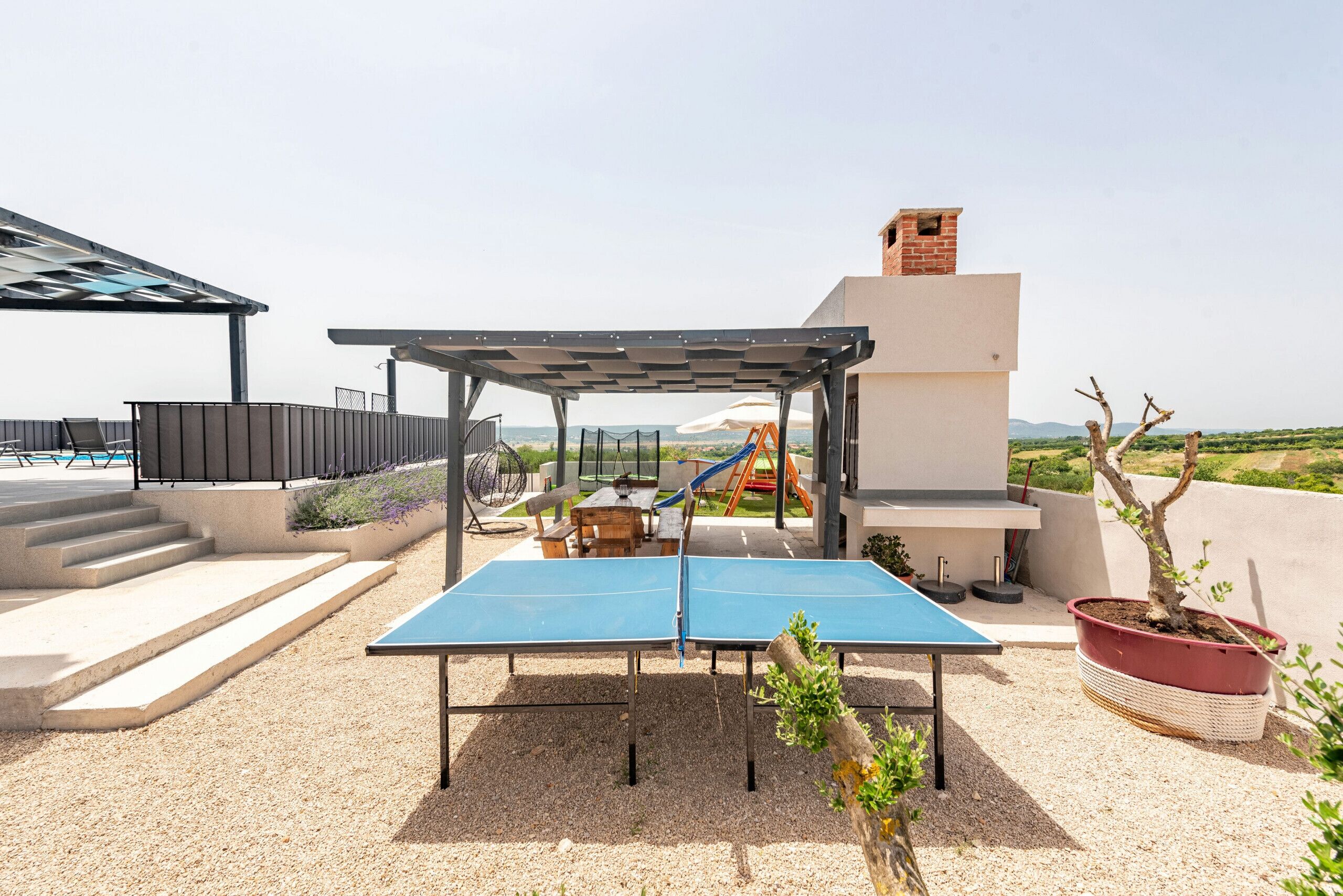 Eine Dachterrasse mit Tischtennisplatte, einer Pergola, einem Spielbereich für Kinder und Blick auf ferne Hügel.