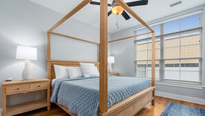 Ein Schlafzimmer mit einem Himmelbett, Nachttischen aus Holz und einem großen Fenster mit Jalousien.