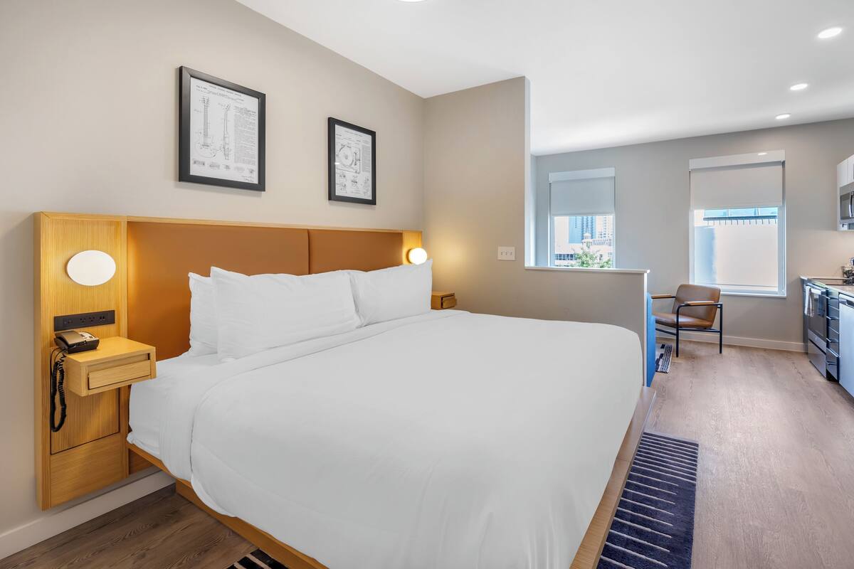 A modern hotel room with a large bed, bedside lamps, a desk with a telephone, and framed certificates on the wall.