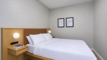 A neatly made bed with a wooden headboard and bedside table, a small bedside lamp, and two framed pictures on the wall.