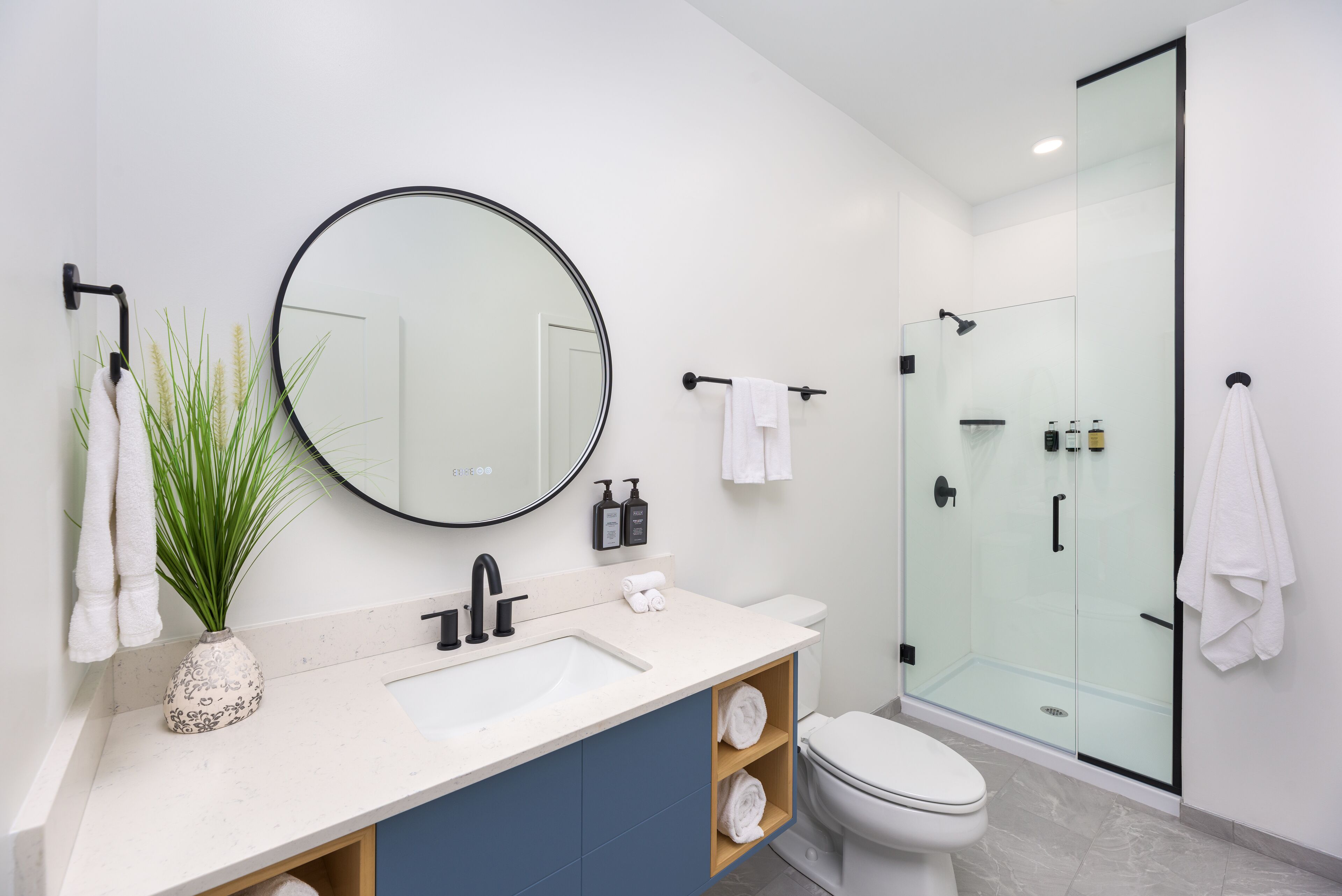 A modern bathroom with a white sink, a round mirror, a glass shower enclosure, and a toilet.