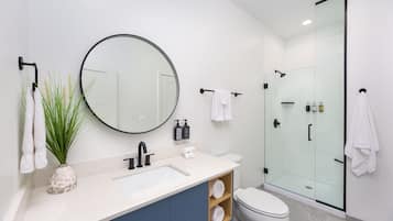 A modern bathroom with a white sink, a round mirror, a glass shower enclosure, and a toilet.