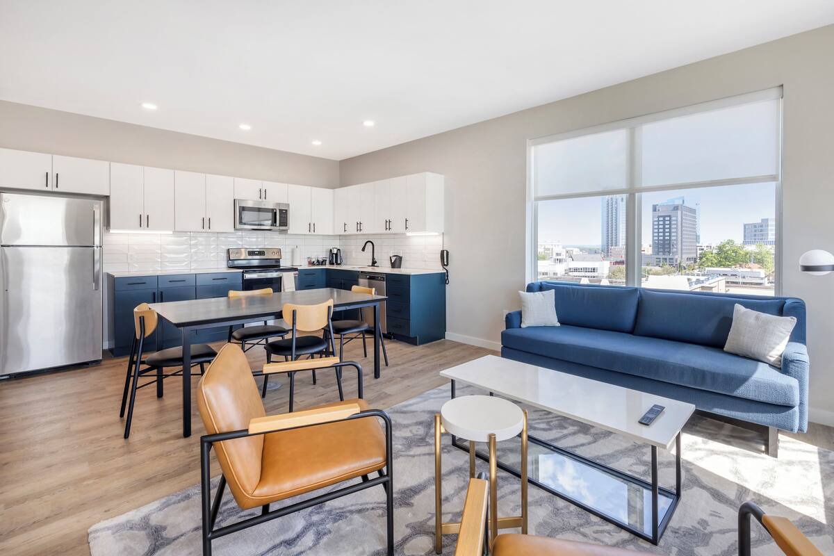 A modern kitchen with white cabinets, a stainless steel refrigerator, and a dining area with a table and chairs.