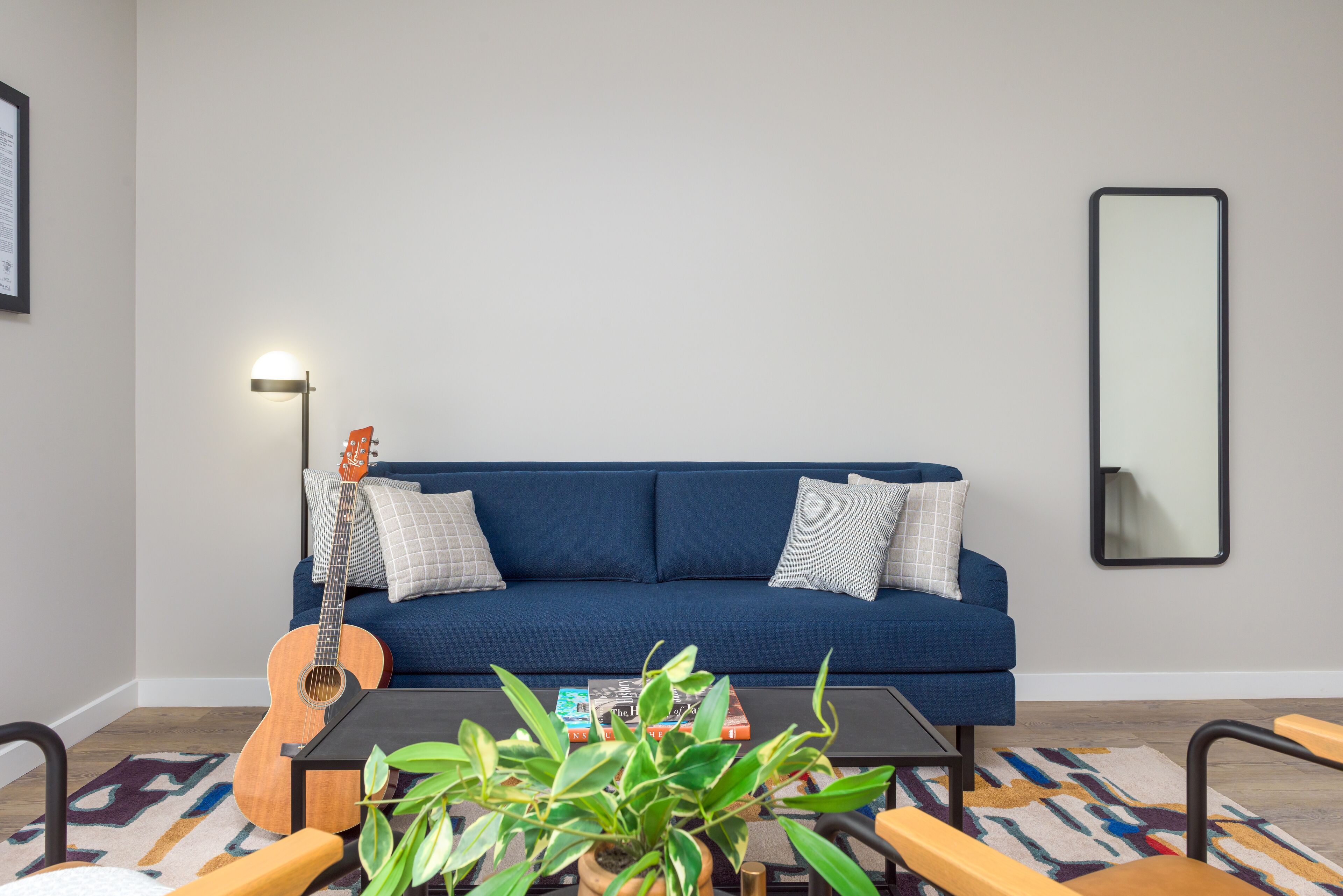 Ein Wohnzimmer mit einem blauen Sofa, einem Couchtisch mit Büchern, einer Gitarre und einer Pflanze.