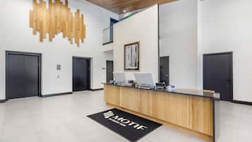 A reception desk with a wooden finish, two computers, and a black doormat with "MOTIF" written on it.
