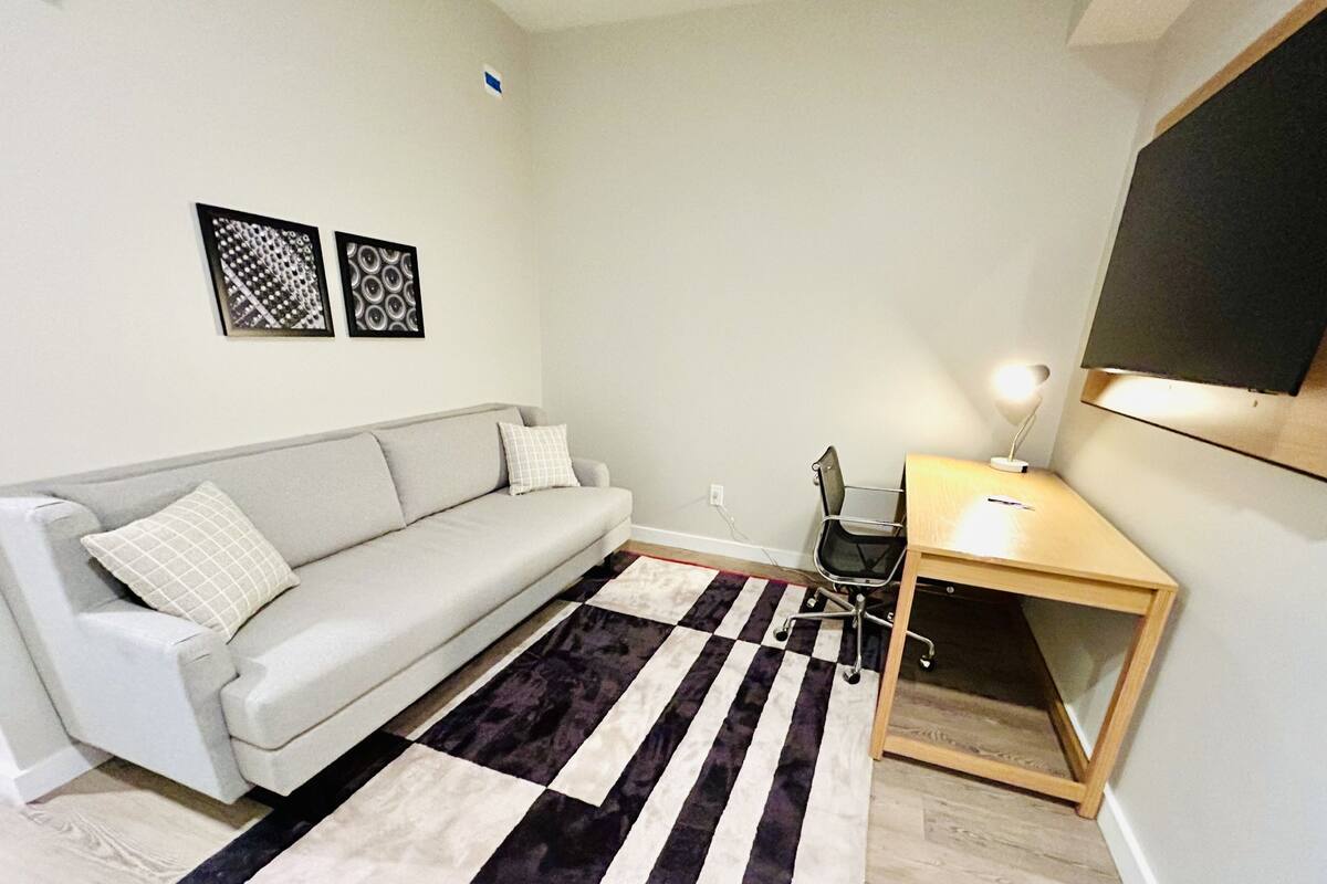 A small, modern living space with a grey sofa, a wooden desk, and a black and white striped rug.