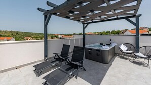 Eine Dachterrasse mit Pergola, zwei Liegestühlen, einem Whirlpool und einem kleinen Tisch.
