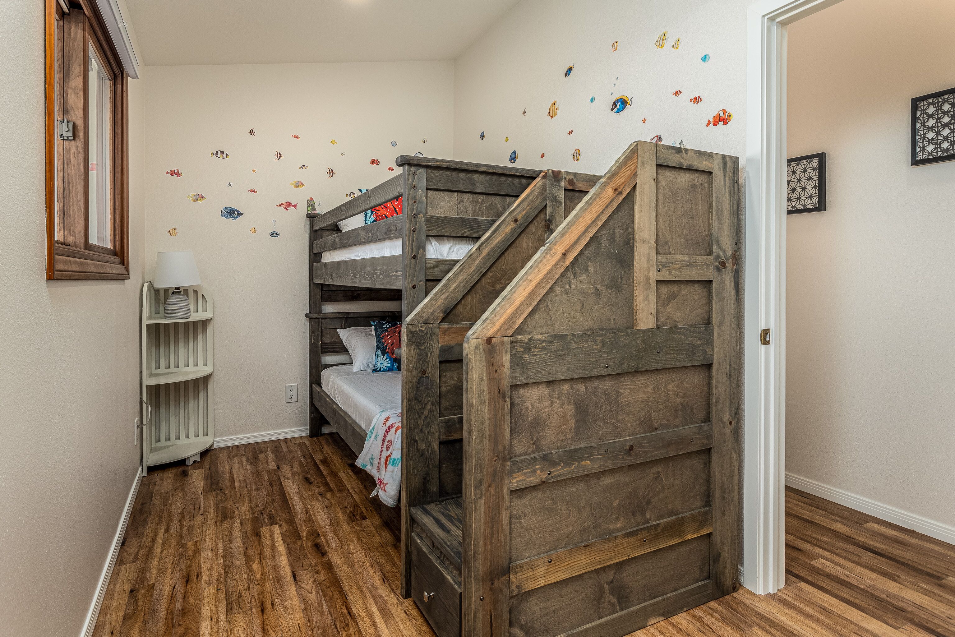 A bedroom with a bunk bed, wooden staircase, and a wall decorated with fish decals.