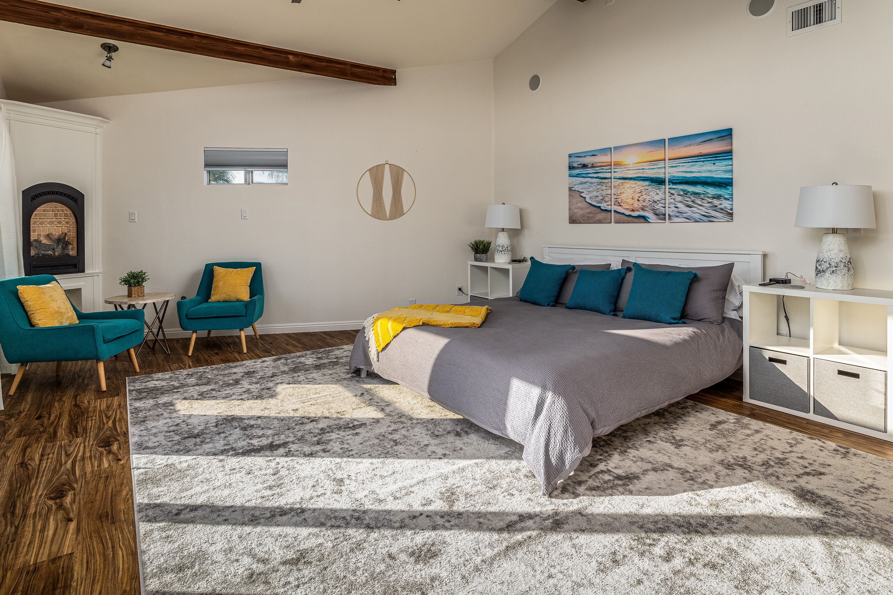 Un dormitorio con una cama grande, dos sillones, una chimenea, un ventanal y un cuadro en la pared.
