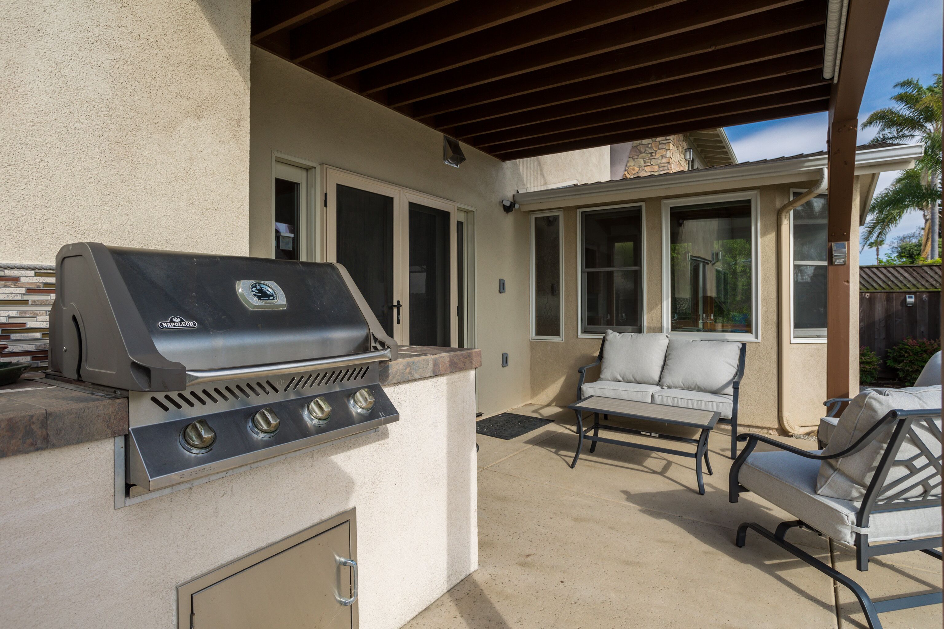 An outdoor patio with a built-in grill, a cushioned seating area, and a stone wall.