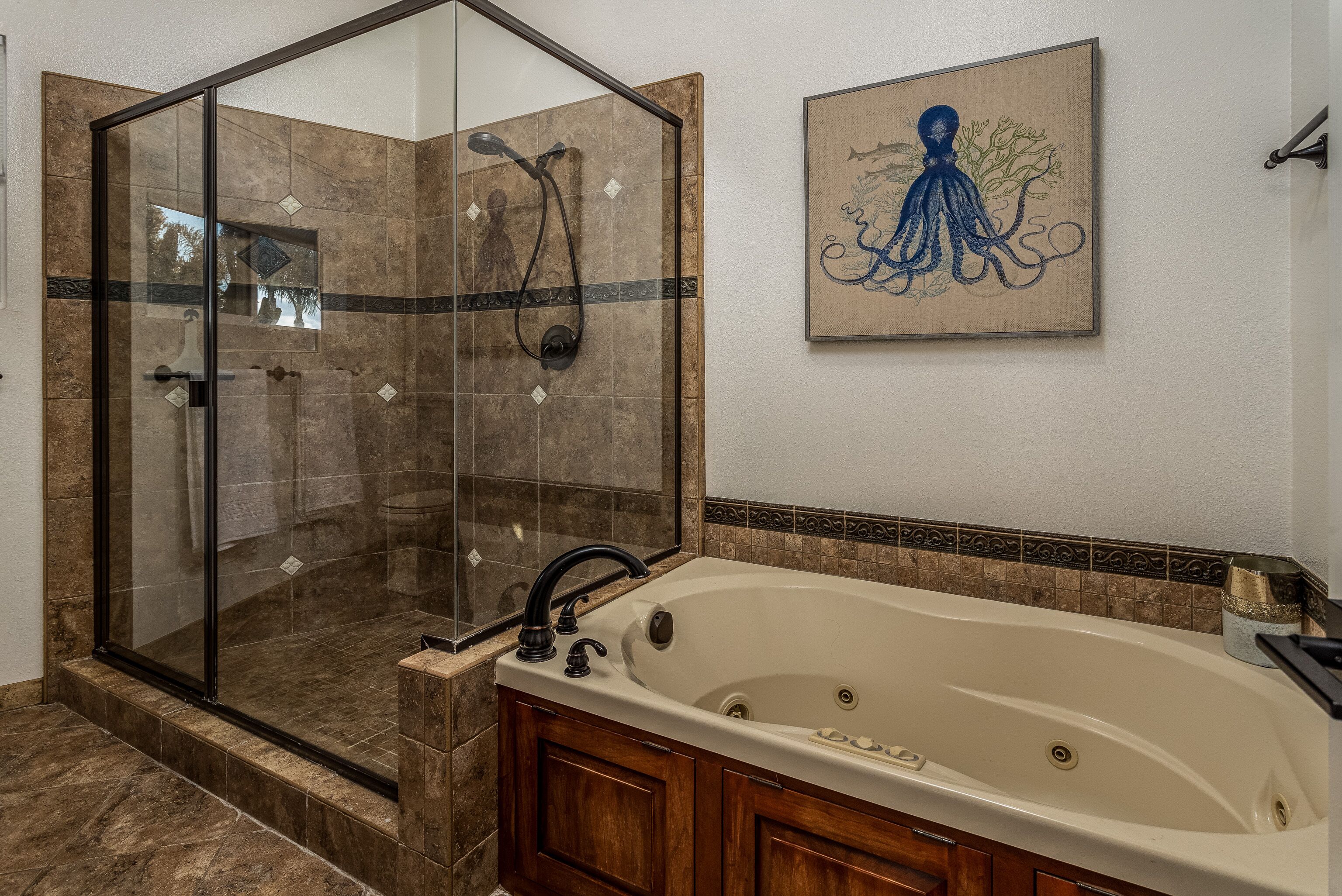 A bathroom with a glass-enclosed shower, a freestanding bathtub, and a wall-mounted artwork of an octopus.