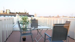 Eine Dachterrasse mit Tisch und Stühlen, einem Blumentopf und Blick auf die Stadtlinie.
