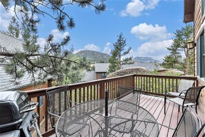 Eine Terrasse mit Grill und rundem Tisch, mit Blick auf eine gebirgige Landschaft.