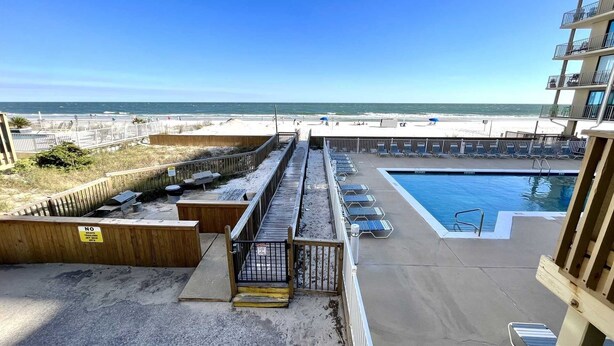 Ett poolområde med utsikt över stranden, ett trädäck och en byggnad med en balkong.