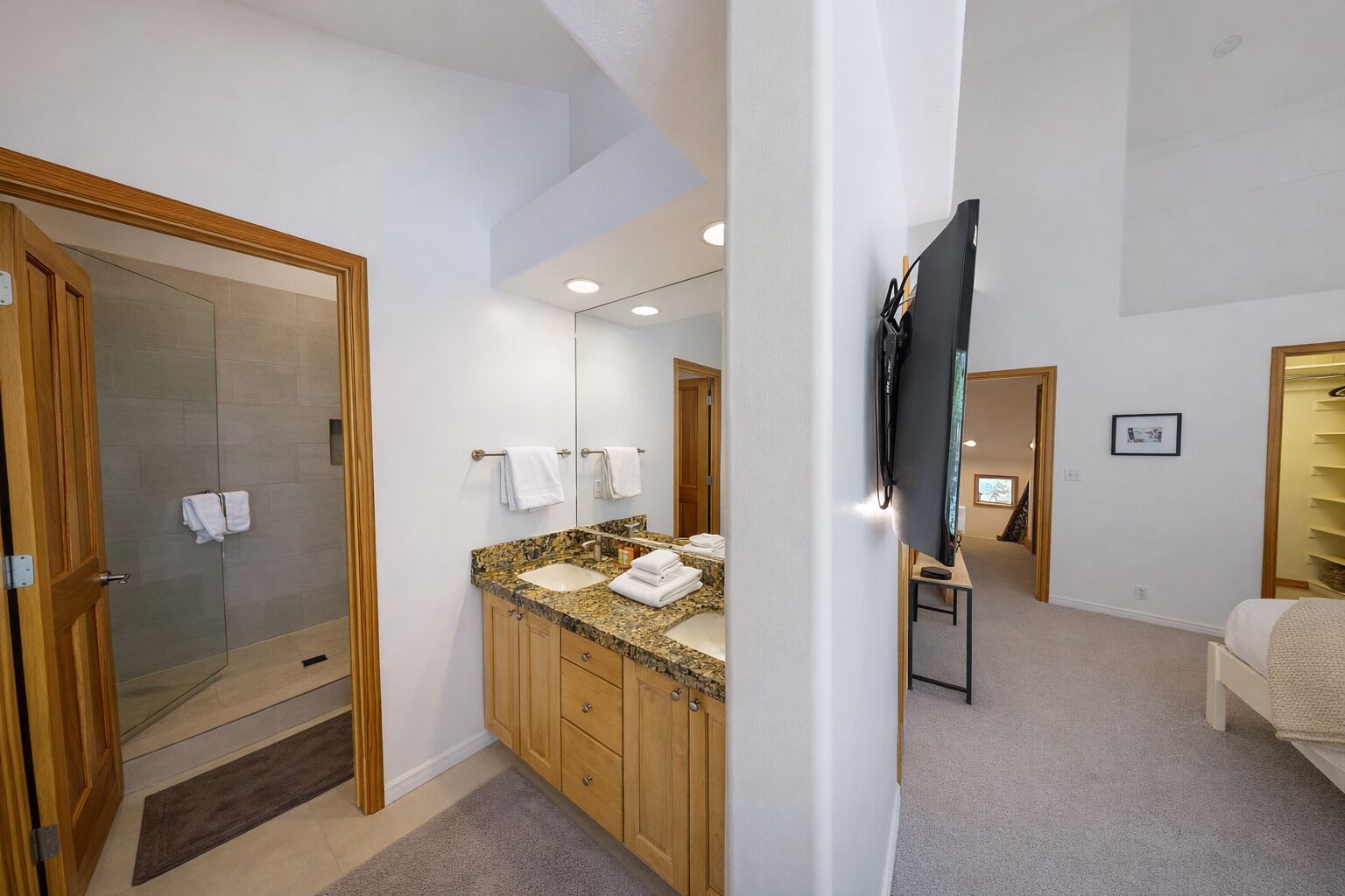 Un baño moderno con ducha, tocador de granito y un espejo grande.