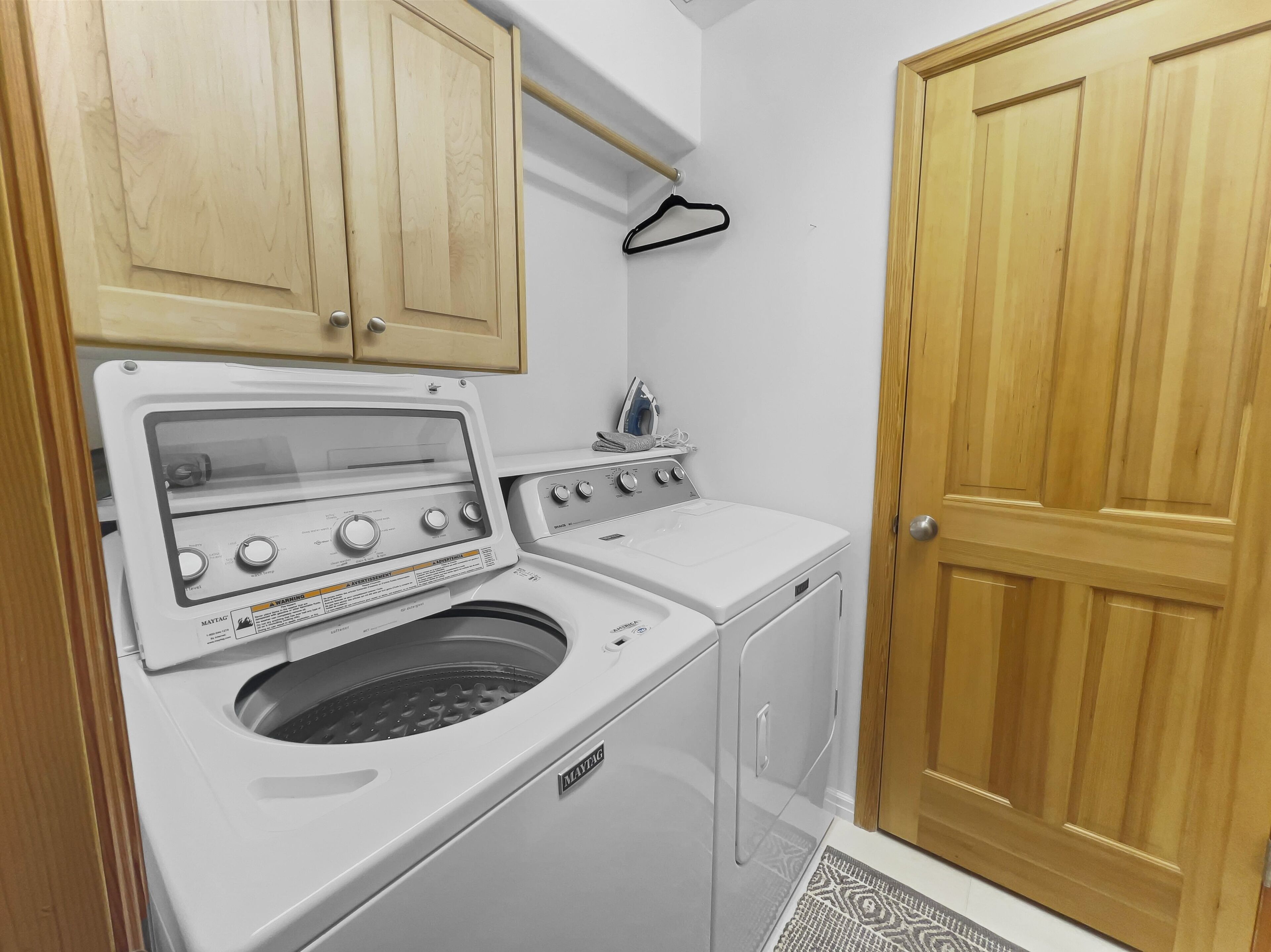 A laundry room with a front-loading washer and dryer, wooden cabinets, a hanging rack, and a wooden door.